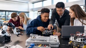 Students and instructor working with small wheeled robots, sensor modules, and robotic arm kit in a bright STEM classroom